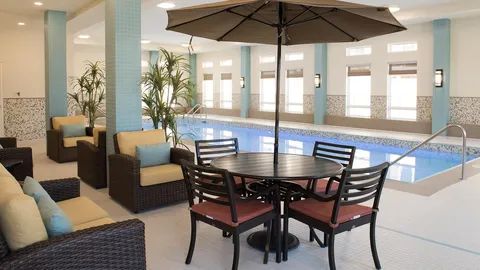 Tables and wicker chairs beneath an umbrella beside an indoor pool