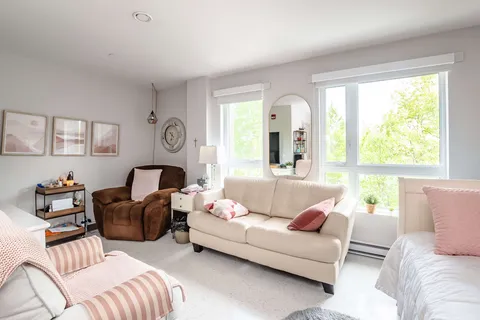 Room with a bed, white sofa, brown armchair, large windows and an oval wall mirror