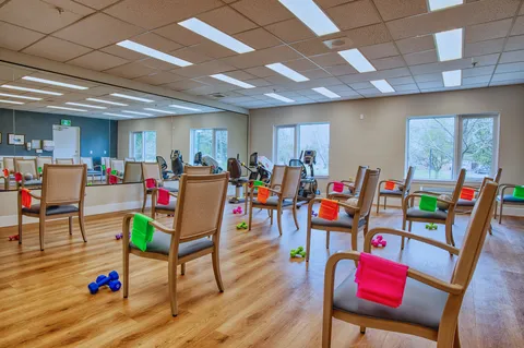 Fitness room with exercise machines, chairs and a mirrored wall.