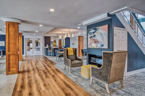 Lounge with upholstered chairs and a fireplace beneath a staircase.