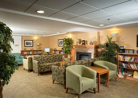 Common room with a fireplace, bookshelves and upholstered chairs.