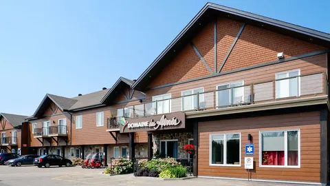 Brown residential building with balconies, a stone entrance, flower beds and parked cars