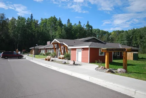 Residence exterior and driveway with red siding and timber columns.