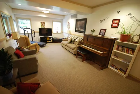 Lounge with sofas, a piano and television beside windows.