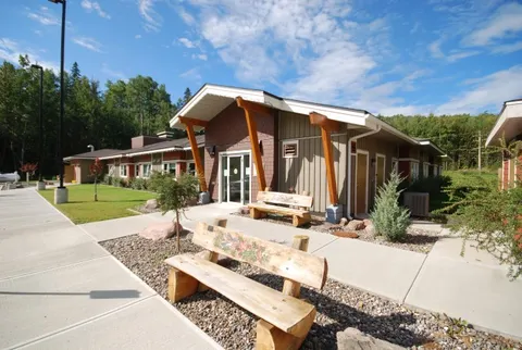 Entrance with timber supports and a bench by planted beds.