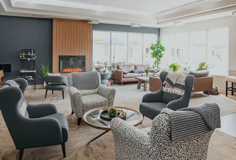 Lounge with patterned armchairs, sofas, plants and a fireplace.