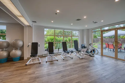 Fitness room with exercise machines and large windows.