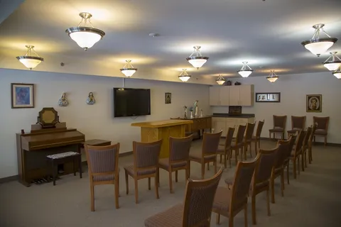 Common room with rows of chairs, a piano and wall television.