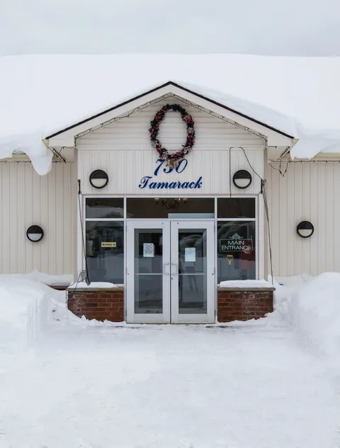 Front entrance with glass doors, a gabled canopy and snow.