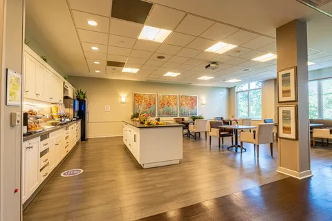 White kitchen cupboards, an island and tables with upholstered chairs