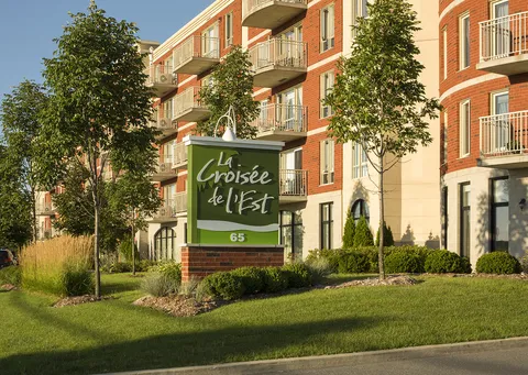 Brick building behind a stone roadside sign and planted garden beds