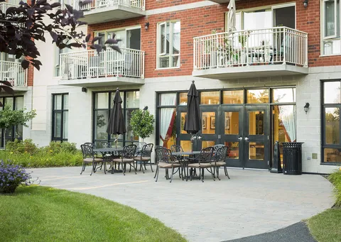 Patio with tables, chairs and folded umbrellas beside glass doors and a lawn