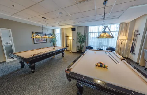 Room with two billiard tables, hanging lamps and windows with sheer curtains