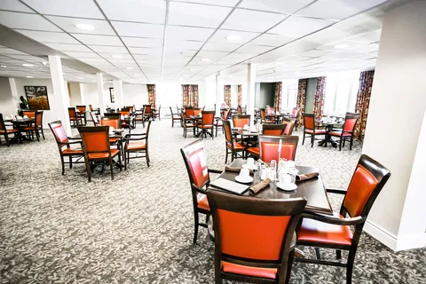 Dining tables with orange upholstered chairs beside large windows