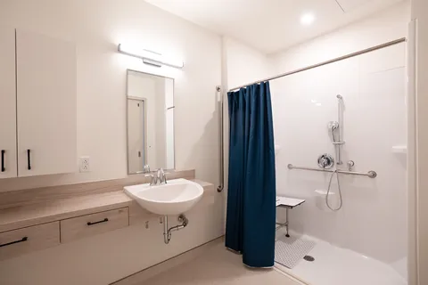 Accessible bathroom with a sink, toilet, grab bars and shower curtain.