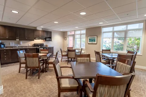 Room with tables and chairs beside a kitchenette and large windows