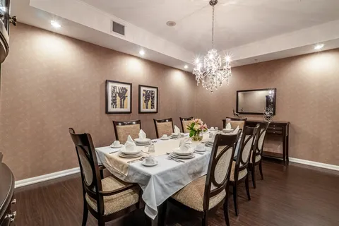 Set dining table with high backed chairs beneath a chandelier
