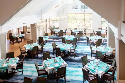 Dining room with set tables, upholstered chairs, large windows and pendant lights