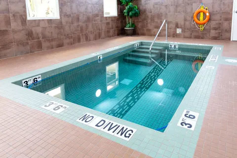 Indoor swimming pool with handrails, tiled walls and windows