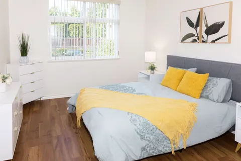 Bedroom with a grey upholstered bed, yellow cushions and a large window