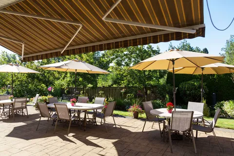 Patio tables and chairs under umbrellas beside a flower garden