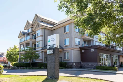 Building with grey siding, balconies, landscaped paths and a freestanding residence sign