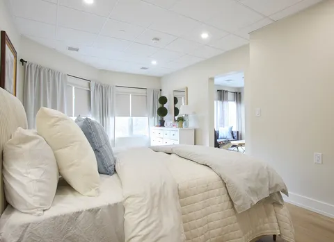 Bedroom with light bedding, a bedside lamp and a dresser