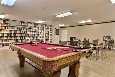 Room with a billiards table, tables and wall-length bookshelves