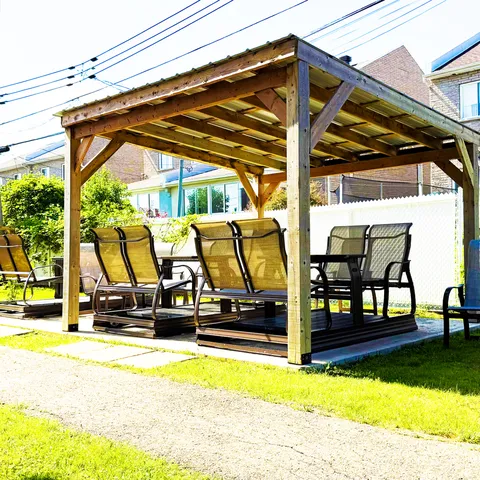 Covered wooden pergola with garden swings beside a lawn.