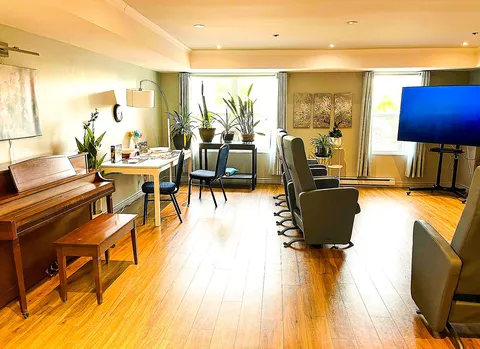 Common room with an upright piano, armchairs and a large television.