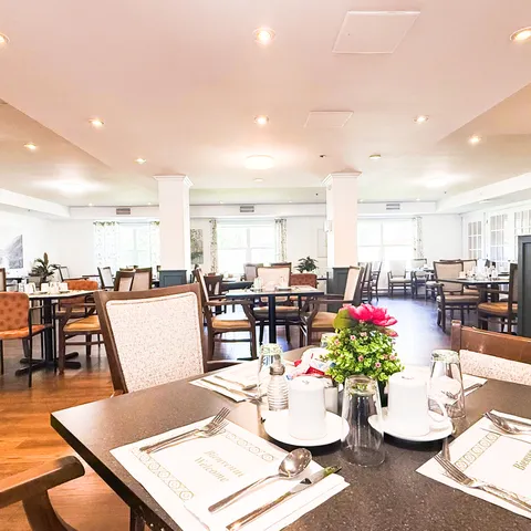 Dining room with set tables, wooden chairs and flowers on the tables.