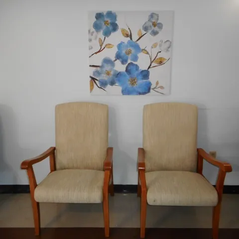 Two upholstered wooden armchairs beneath a blue flower painting
