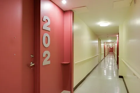 Hallway with a red door numbered 202 and wall rails