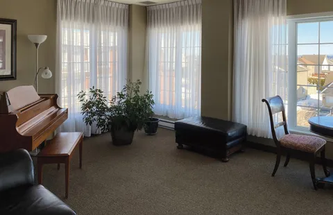 Room with an upright piano beside large windows.