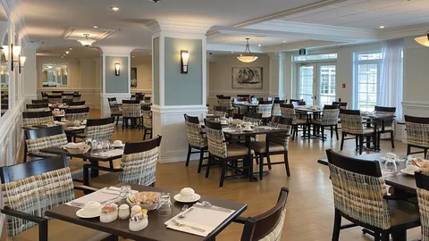 Dining room with rows of tables and upholstered chairs.