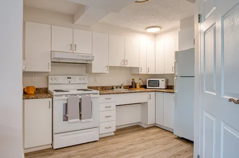 Kitchen with white cabinets, stove, refrigerator and sink.