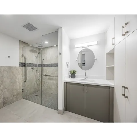 Bathroom with a round mirror, a vanity and a tiled shower