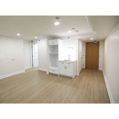 Unfurnished room with wood flooring, a kitchenette and a wooden entrance door