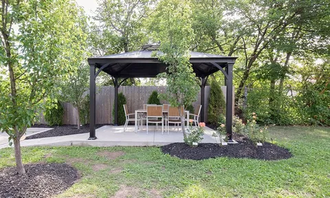 Outdoor dining patio beneath a pergola beside a lawn.