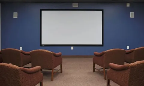 Screening room with upholstered chairs facing a projection screen.