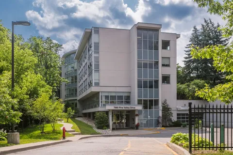 Multi-storey building with a glass-fronted entrance, trees and a driveway