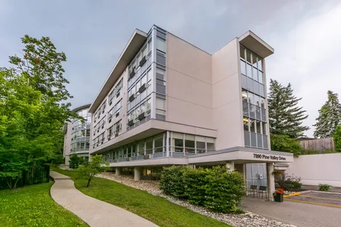 Multi-storey building with rows of windows and shrubs beside the entrance