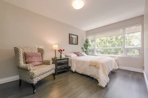 Bedroom with a bed, upholstered chair, bedside table and large window