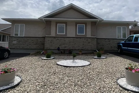 Residence front with stone-facing walls, a gravel garden, flowerpots and parked vehicles