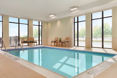 Indoor swimming pool with large windows and poolside chairs.