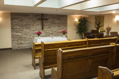 Chapel with wooden pews beside an altar and wall cross.