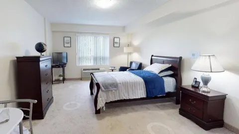 Studio bedroom with a bed, dresser, lamps and window.