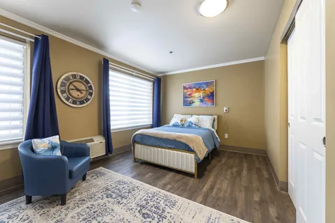 Bedroom with blue bedding, an armchair, two windows and a sailboat painting
