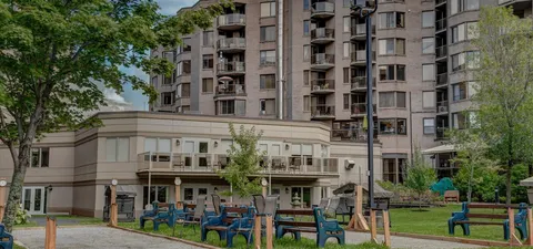 Residence building beside lawns, trees and garden seating.