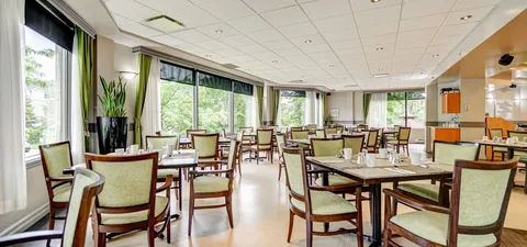 Dining room with tables and chairs beside large windows.